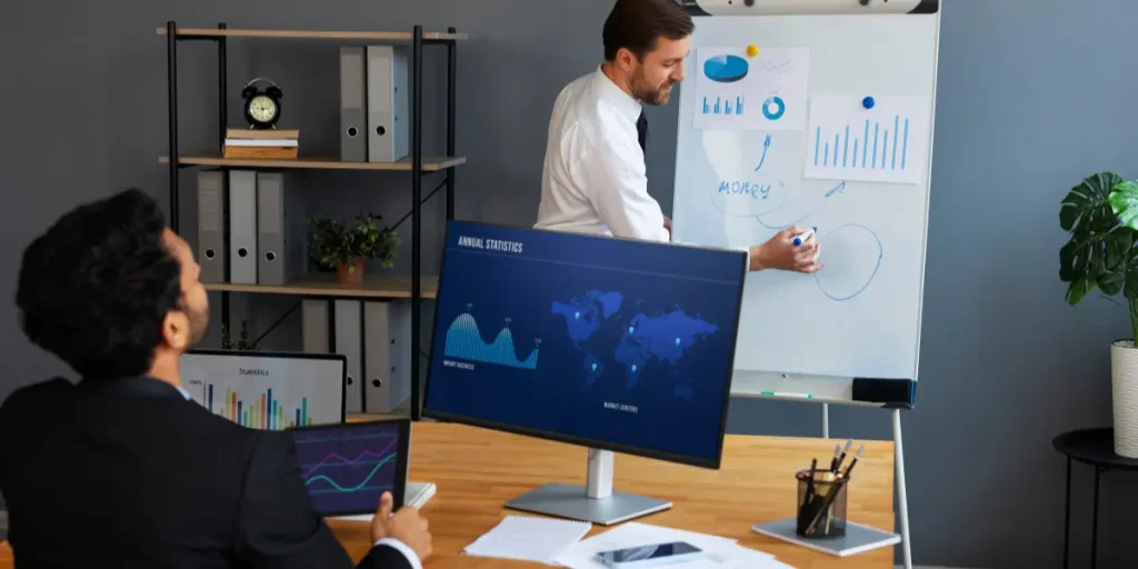 Marketing expert presenting data-driven performance marketing strategies on a whiteboard while a business professional analyzes digital analytics on a screen.