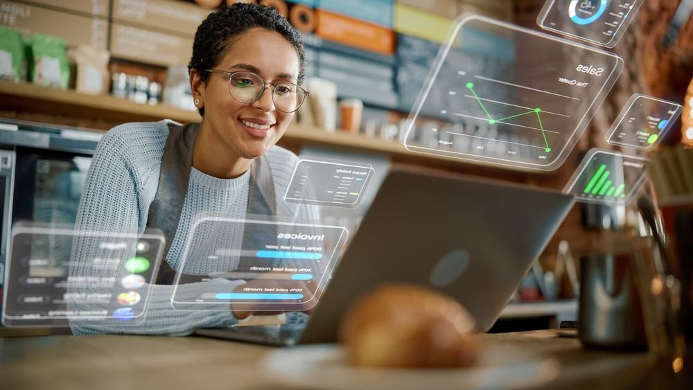 Smiling small business owner using digital tools and analytics on a laptop in a modern café, representing IT and digital solutions for business growth in Colorado Springs.